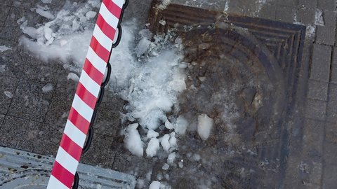 Wet snow with ice and icicles lies on the sidewalk that has fallen from the rear roof. Warning tape to avoid injury from icicles, outdoor