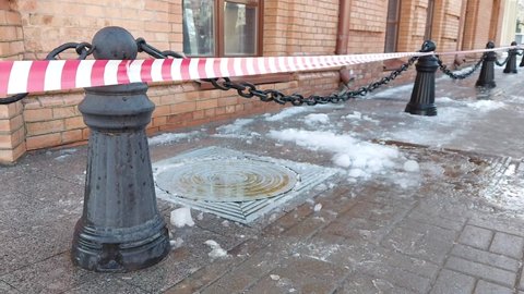 Red and white warning tape in the city near a building from the roof of which ice and icicles are falling. Risk of injury, weather