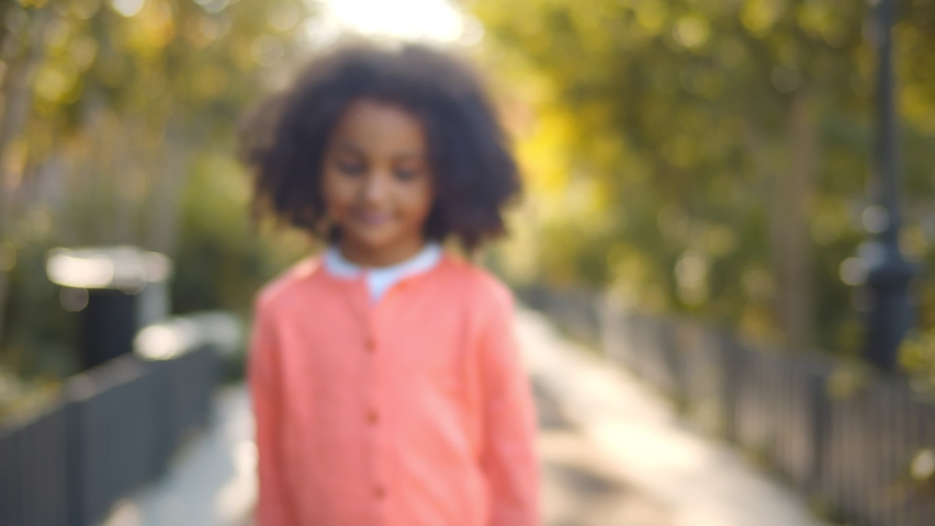 Close up of happy cute little african girl smiling at camera outdoors. Portrait of adorable preschool afro-american kid smiling standing in park over blurred background Royalty-Free Stock Footage #1067145592