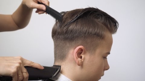 Cutting the hair at the back of the head with a hair clipper. The boy has a haircut at the barbershop. Men's haircut.
