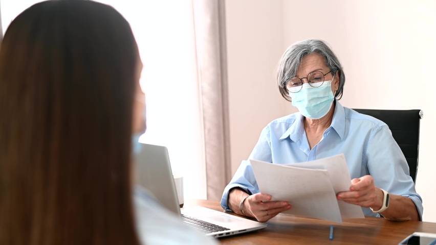 Senior elder businesswoman hr manager wearing a face mask, interviewing a job seeker, mentoring student, consulting and teaching a new young female team member. Social distancing and safety concept