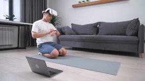 Young man in virtual reality glasses performs a plank, sports using modern technology in self-isolation, fitness training online.