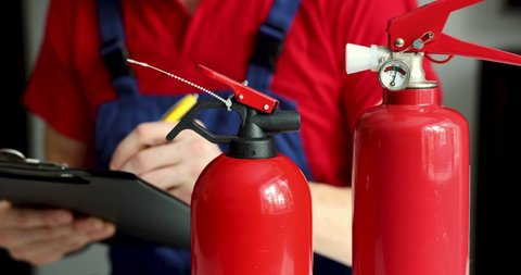 fire safety and equipment maintenance service - man checking extinguisher condition and writing documents