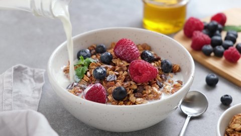 Granola bowl with berries and milk. Pouring milk into breakfast cereals. Healthy food, clean eating concept