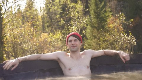 Young man enjoy spending time in bath outdoors in the forest, relax hot water inside of bath.