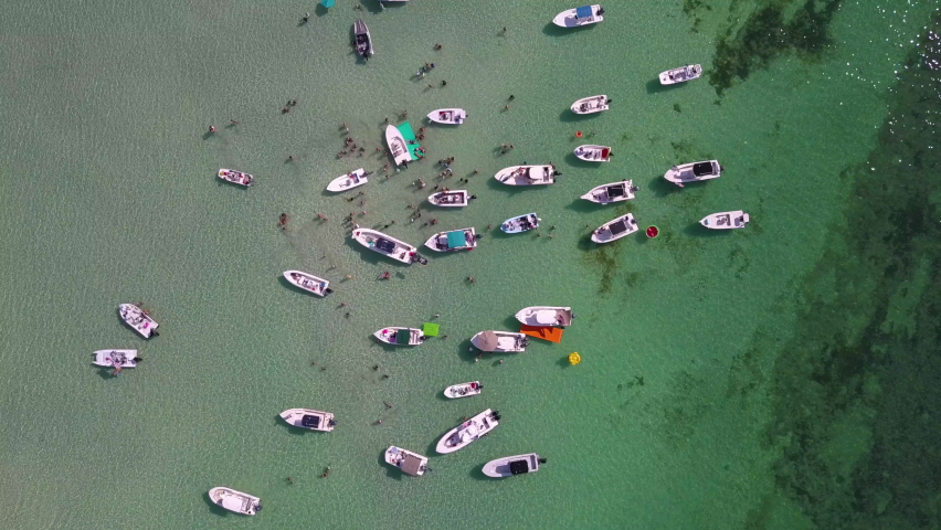 A "pushing-in" style, downward drone view of clear turquoise water, tropical paradise vibes, and a bunch of party boats anchored on Snipes Key Sandbar near Key West in the Florida Keys.