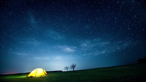 Glowing camping tent in the night mountains under the twinkling starry sky. Cinemagraph.