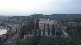 Panoramic evening aerial view of Verona ancient city. The drone approaches the river Adige, the typical Italian apartment rooftops and bridge Ponte Pietra. Video in 4K