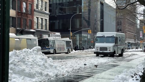 NYC, USA - FEB 3, 2021: piles of snow in Manhattan winter - Grub Hub delivery man riding bicycle in street slush New York City.