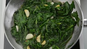 Preparing garlic sauteed spinach dish in a saucepan