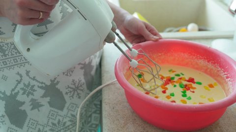 Women's hands, knead the dough on the cake, adding candied fruits to it. Sweet pastries. A woman whips the dough with a mixer.