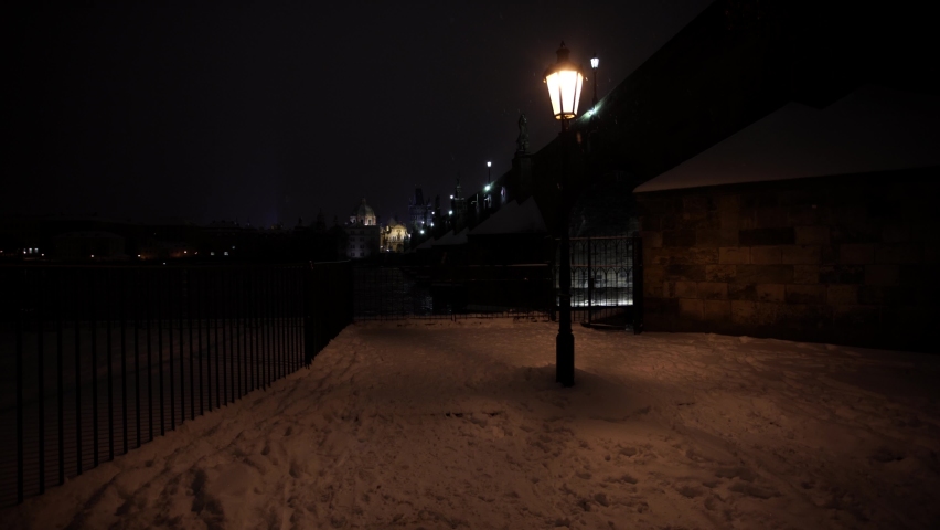 
Close-up bright illuminated streetlight lantern. shining lantern on street lights at night. In the background is an illuminated stone Charles Bridge on the Vltava river at night and falling snow