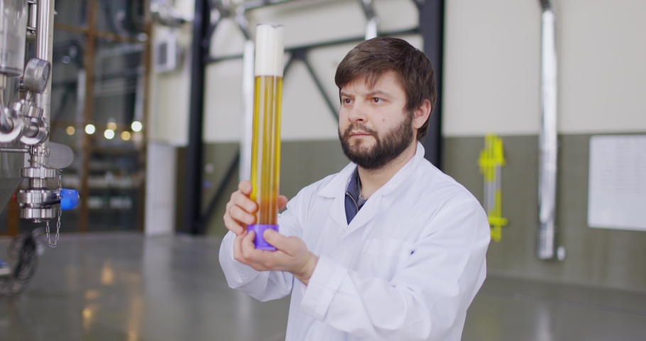 Men testing quality of fresh beer in a brewery. Brewer dressed in lab coat tasting beer from glass