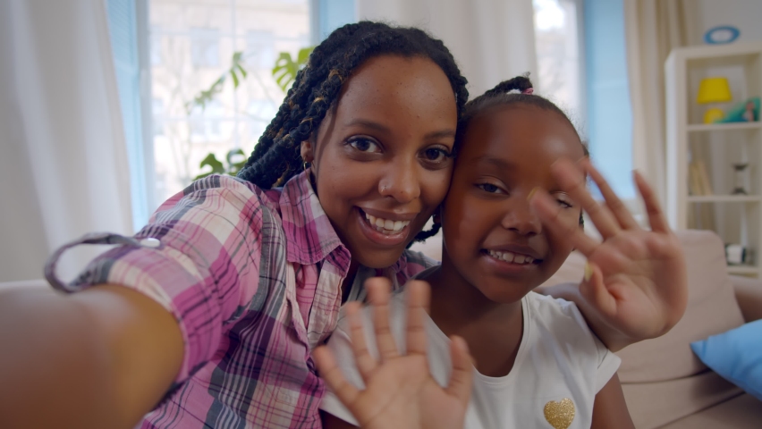 Happy african mother and little daughter making video call at home. Cheerful afro-american sisters waving hands having video conference or filming video for internet blog Royalty-Free Stock Footage #1067174305