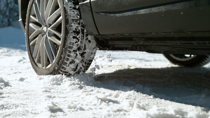 SLOW MOTION, LOW ANGLE, CLOSE UP, DOF: Car's wheels spin in place and spew up pieces of white snow as it attempts to gain traction on the slippery road. Snow flies up from a vehicle's spinning wheel.