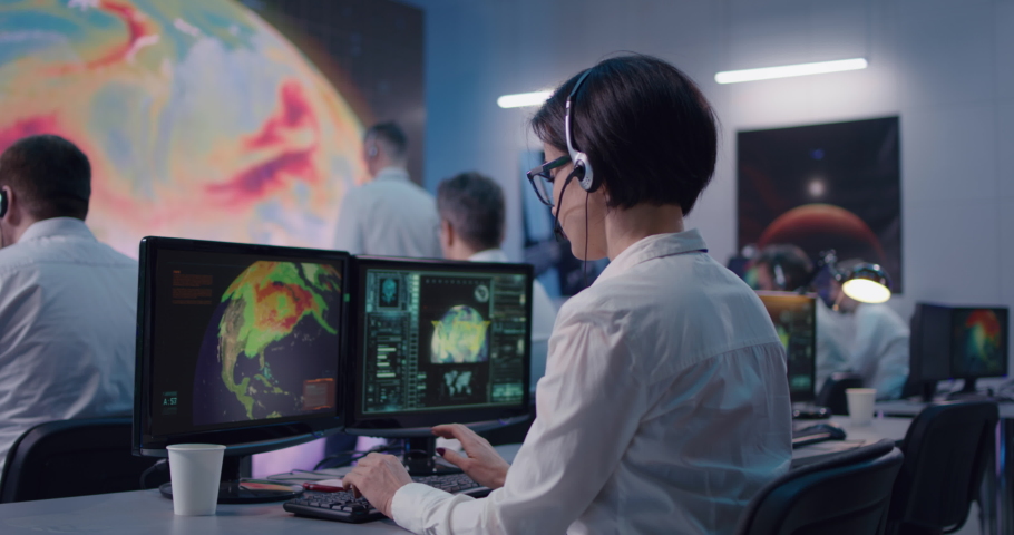 Zoom out view of young woman with headset typing on computer keyboard while researching global warming with team in office of ecology control center