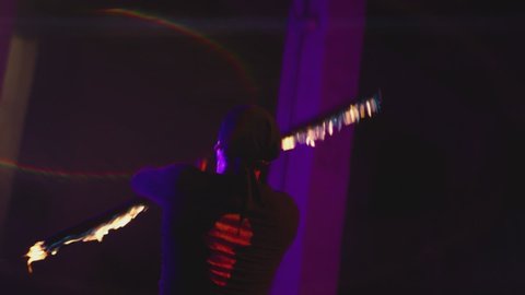 Adult man with bandanna dressed in black performing cool and dangerous fire show, doing many tricks with fire baton staff ignited from both sides each at night. Abandoned dark building slow motion 