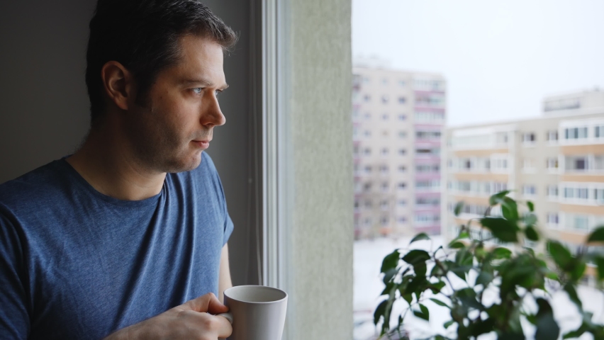 Man with cup of tea looks out the window.
