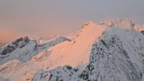 A morning flight over a mountain in Lofoten Island. Areal view of massive snowy peaks. Soft light at a sunrise.