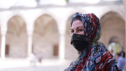 A woman in a headscarf and a protective mask walks in a mosque on a sunny summer day