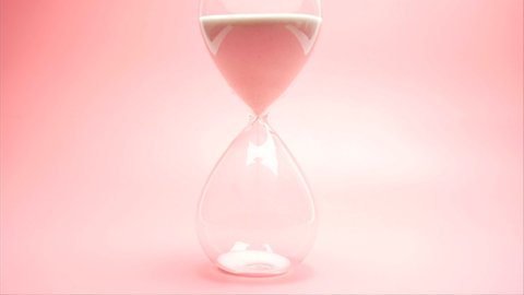 Sand pouring in hourglass on pink background, time pass concept, deadline end.