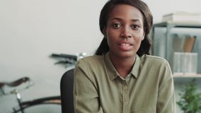 Close up of young beautiful african american woman sitting in office and talking while looking at camera. Interview online. Coach consultation remotely.