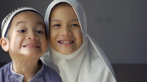 Closed up shot of Asian Muslim kids.young sister and brother sibling in Muslim traditional dress.Happy and looking to camera.Concept of happy kid in Ramadan or family bonding.