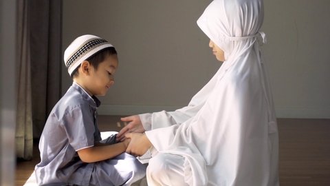 The warm climate of Asian Muslim family.Muslim kids in traditional clothing greeting to elders,father by touch his hand and smiling.Concept of Muslim family greeting by touching their hands and face.
