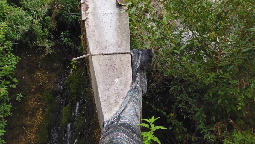 Old, craft laundry facility. The outdoor trough is filled with water from a pipe wrapped in a rug. Mountain water flows over rocks, vegetation.
