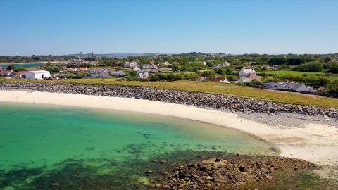 sweeping drone footage of Guernsey coastline, stunning golden beach and clear calm sea on sunny summer day and only one man and his dog on the beach.Cottages and Peninsula Hotel in the background.