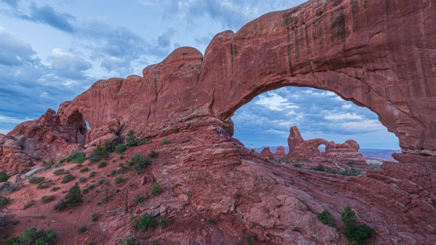 Golden sunrise time lapse with light beaming on unique arch geological formations and flowing clouds at the Windows and Turret Arch in Arches National Park, Utah United States.