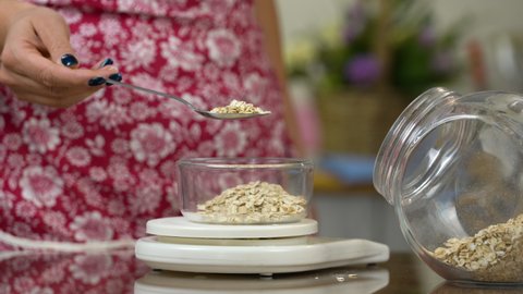 Oatmeal on kitchen scales․ Woman's hand is pouring oat groats in transparent bowl on kitchen scale. Healthy eating concept. Diet and calories counting concept. 