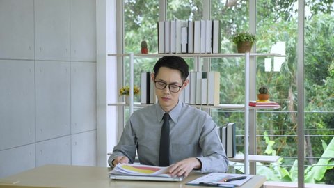 Slow-motion, medium shot of a young Asian male entrepreneur or businessman sitting, working in the office, working, being disappointed and angry, losing temper, and throwing documents away in the air