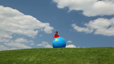 boy rolling inflatable ball in meadow towards camera