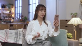 waist up asian female ceo sitting in living room with phone in hand making her points clear with gestures in a video conference.
