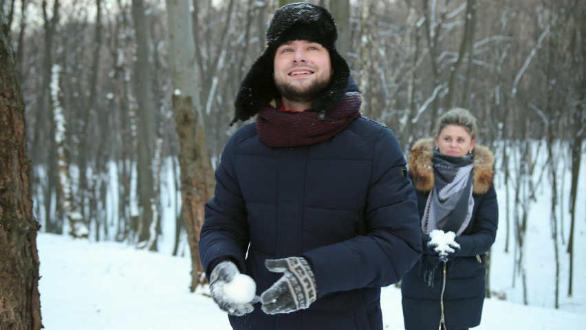 Pair having a snowball fight. Winter fun. Woman plays throwing snow at friend face, enjoying cold season. Happy and joyful concept. Young couple is playing snowballs