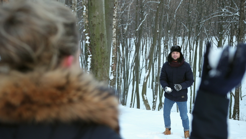 Pair having a snowball fight. Winter fun. Man plays throwing snow at friend face, enjoying cold season. Happy and joyful concept. Young couple is playing snowballs