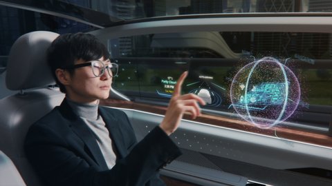 Futuristic Concept: Japanese Businessman Checking Arrival Location on an Interactive Augmented Reality 3D Navigation App while Sitting in on the Back Seat of an Autonomous Self-Driving Car with VFX.