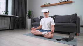 Cheerful man in virtual reality glasses meditates in the living room, modern technology and augmented reality, a man rests on self-isolation.