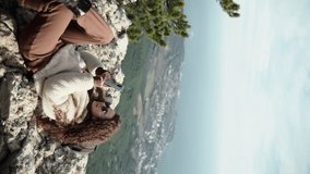 Vertical footage. beautiful young stylishly dressed girl in sunglasses lies resting on the edge of a cliff and looks into a smartphone. The modern traveler on a halt uses the Internet in nature. 5g