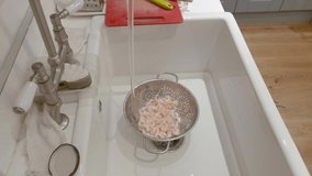 Prawns or shrimp defrosting under a tap in a strainer, in a kitchen sink