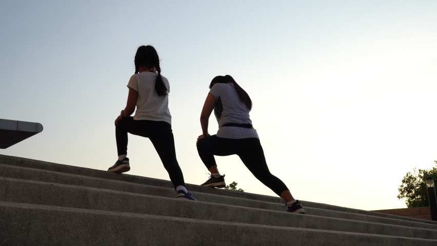Asian family, mother and daughter athlete stretching legs on city stairs for warming up before running.
