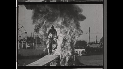 1950s Los Angeles, CA. Stuntman and Daredevil Jumps Ramp to Ramp through Fire Explosion on Motorcycle Bike in Evel Knievel like Stunt. 