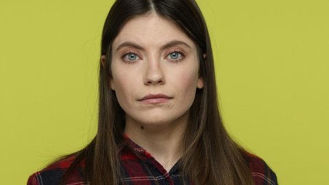 Portrait curious brunette young adult woman looking into camera through magnifying glass, inspecting something, spying on boyfriend, private detective. Indoor studio shot isolated on yellow background