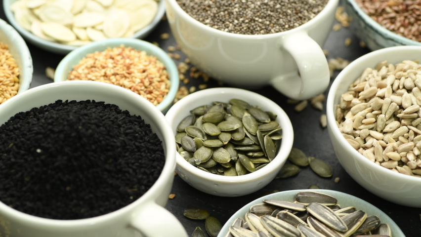 Assortment od healthy seeds - sesame, flax seed, sunflower seeds, pumpkin seed, chia and black seed in bowls on a black stone background | Shutterstock HD Video #1067219899