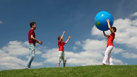 parents and son playing with big inflatable ball in a meadow