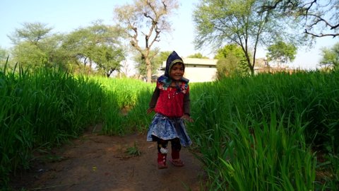08 February 2021- Khatoo, Jaipur, India. Pretty little Indian girl running on meadow behind strong sunlight. Winter season and traditional attire.