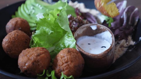 Close up of fork dipping a falafel in creamy vegan sauce. Healthy organic plant based plate