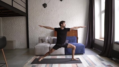 Man practice warrior yoga pose in own living room on mat