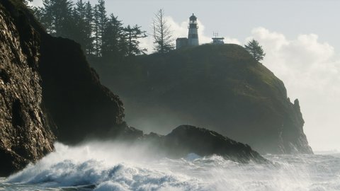 Massive King Tide Waves Crashing on Washington Coast with Lighthouse Background. Slow motion white spray mist from ocean water colliding with Pacific Northwest coastal cliffs